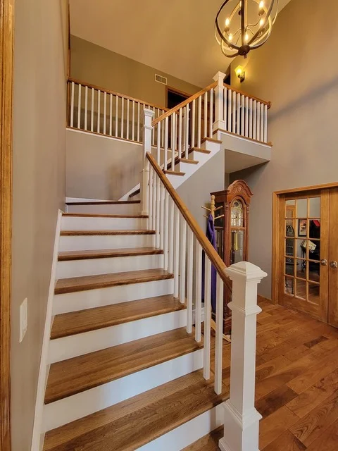 Two-story staircase with wood treads, white risers, and white spindle railings