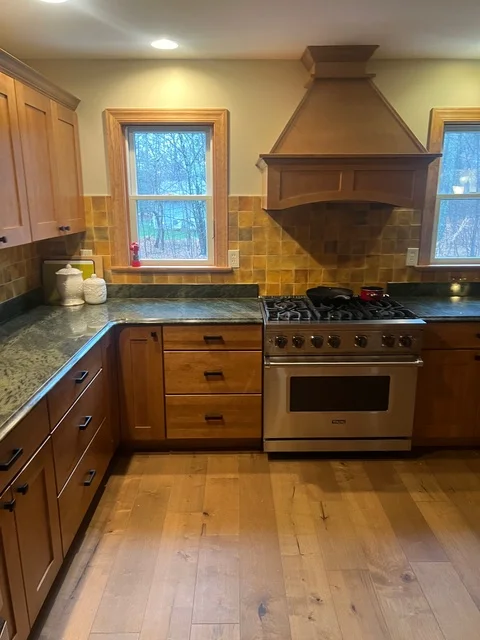 Kitchen with wood cabinets, granite counters, stainless steel range, tile backsplash, and wood flooring
