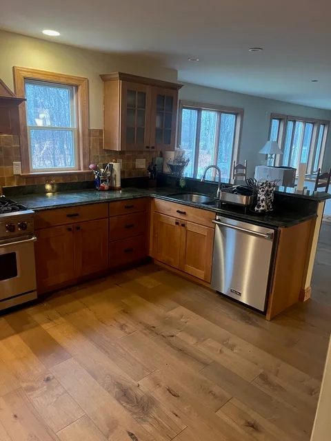 Kitchen with cherry cabinetry, black granite counters, stainless steel appliances, and wood flooring