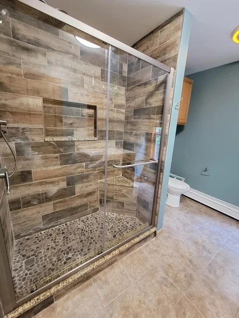 Frameless glass shower with wood-look tile walls and pebble stone floor