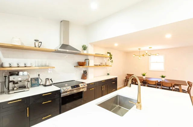 Modern kitchen with black and wood cabinetry, white quartz counters, stainless steel appliances, and brass fixtures