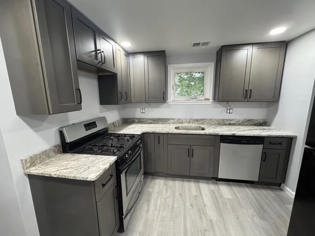 Gray kitchen cabinets, granite counters, gas range, stainless steel appliances, vinyl plank flooring