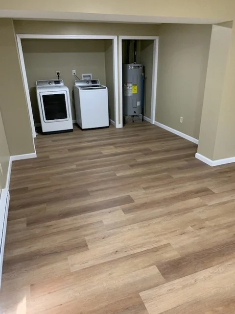 Luxury vinyl plank flooring in laundry room with washer, dryer, and water heater