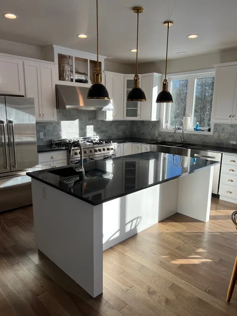 White kitchen with black quartz island, stainless steel appliances, gray tile backsplash, and brass pendant lights