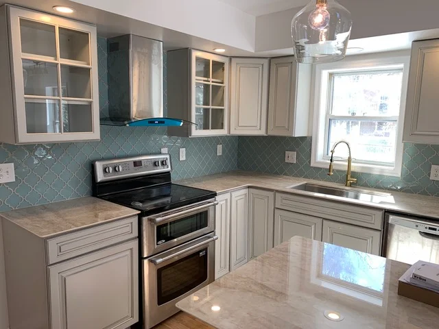 Kitchen with cream cabinets, quartz counters, turquoise quatrefoil backsplash, stainless steel appliances