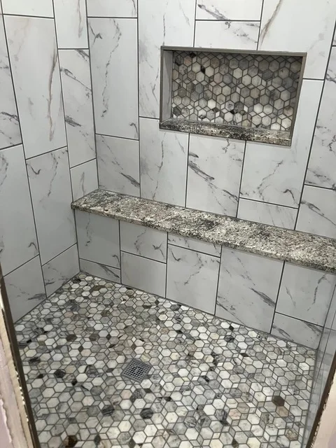 Marble subway tile shower walls with hexagonal mosaic floor and granite shelf