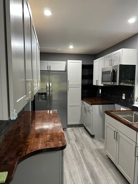 Modern kitchen with white cabinets, wood countertops, stainless steel appliances, and gray flooring