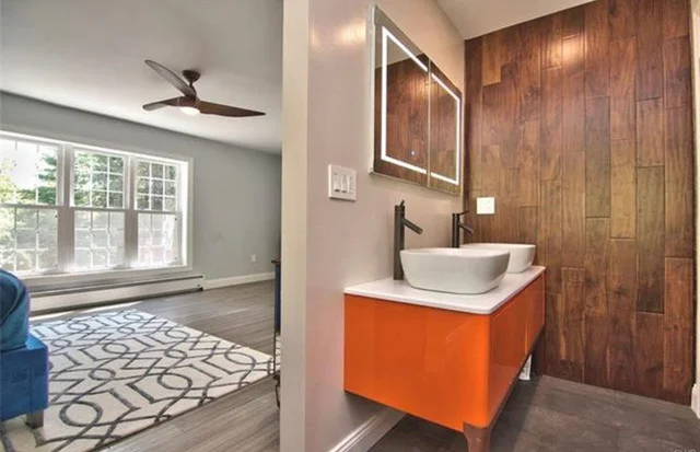 Bathroom vanity with orange cabinet, white sink, wood tile backsplash, and framed mirror