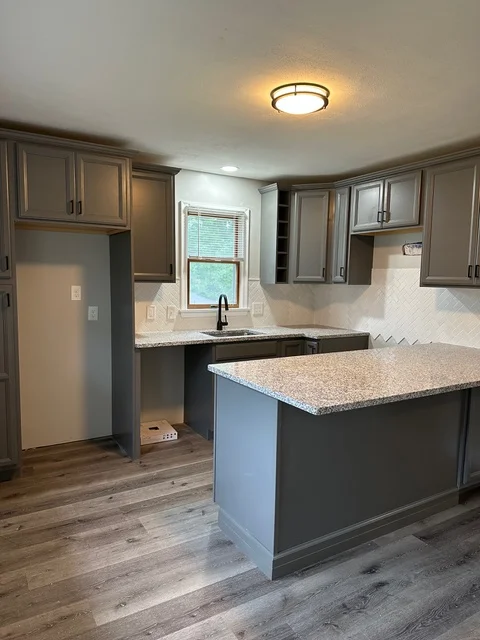Modern kitchen with gray cabinetry, granite counters, island, subway tile backsplash, and vinyl plank flooring