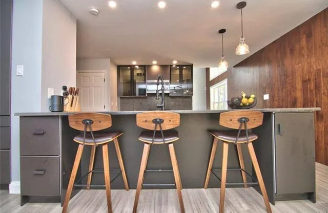 Modern kitchen with gray island, wood bar stools, pendant lights, and wood accent wall