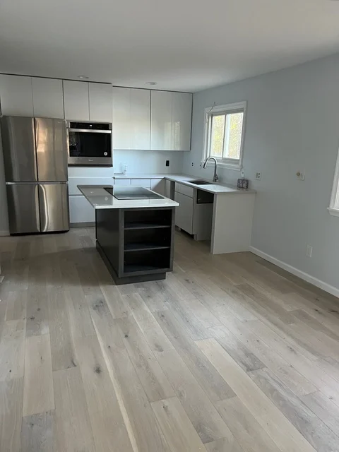 Modern kitchen with white cabinets, stainless steel appliances, center island, and light wood flooring